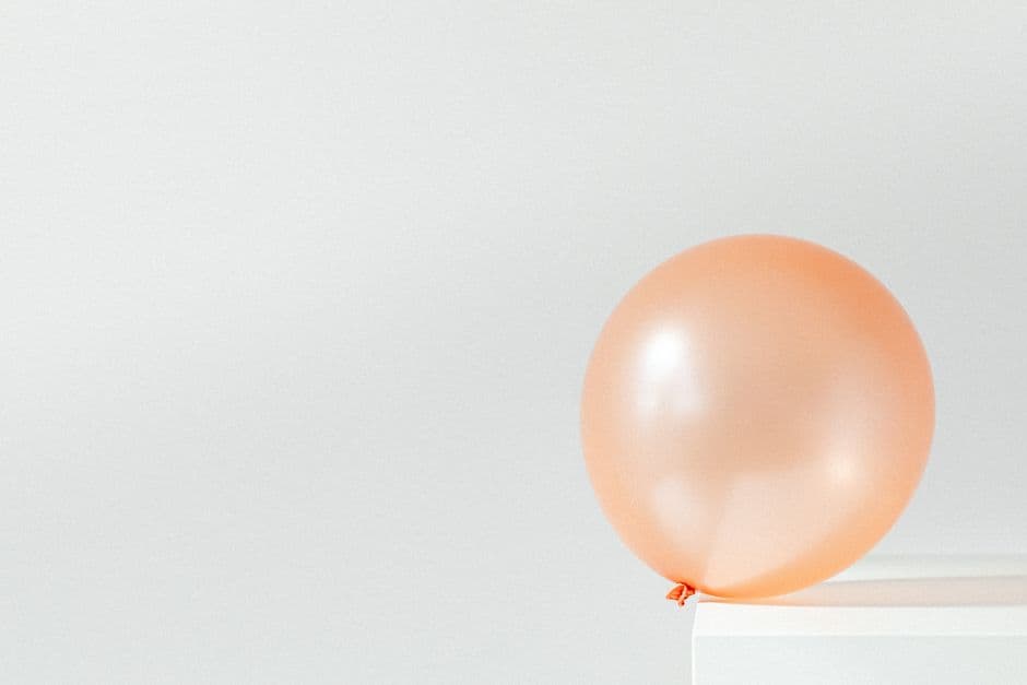 A minimalistic image featuring a single orange balloon on a white surface against a plain background.