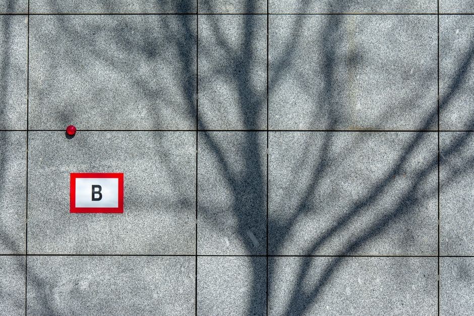 Artistic shadow of tree branches on a tiled wall with a marked letter B.