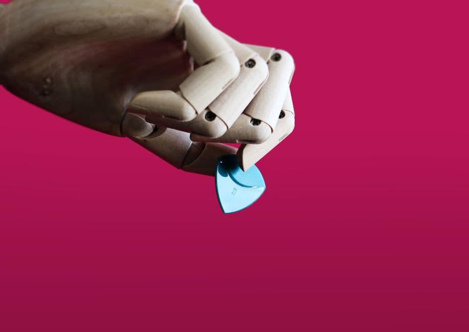 Close-up of a wooden hand with a blue guitar pick against a vibrant red background.