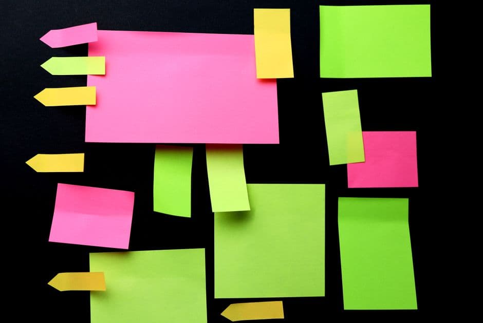 Bright pink, yellow, and green sticky notes arranged geometrically on a black background.