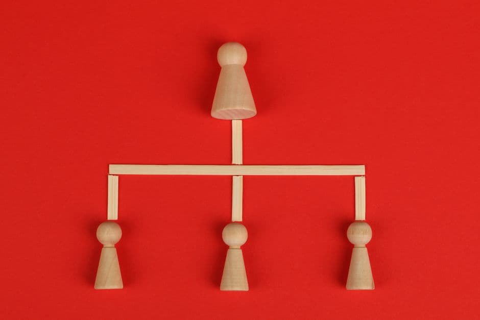 Conceptual depiction of hierarchy using wooden pieces on a vibrant red background.
